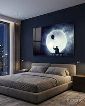 Moon Dreamer glass wall art displayed above a grey upholstered bed in a dark navy bedroom with city view