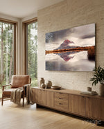 Mountain glass wall art displayed above a walnut credenza in a warm travertine-walled lounge with cognac armchair and stoneware vases
