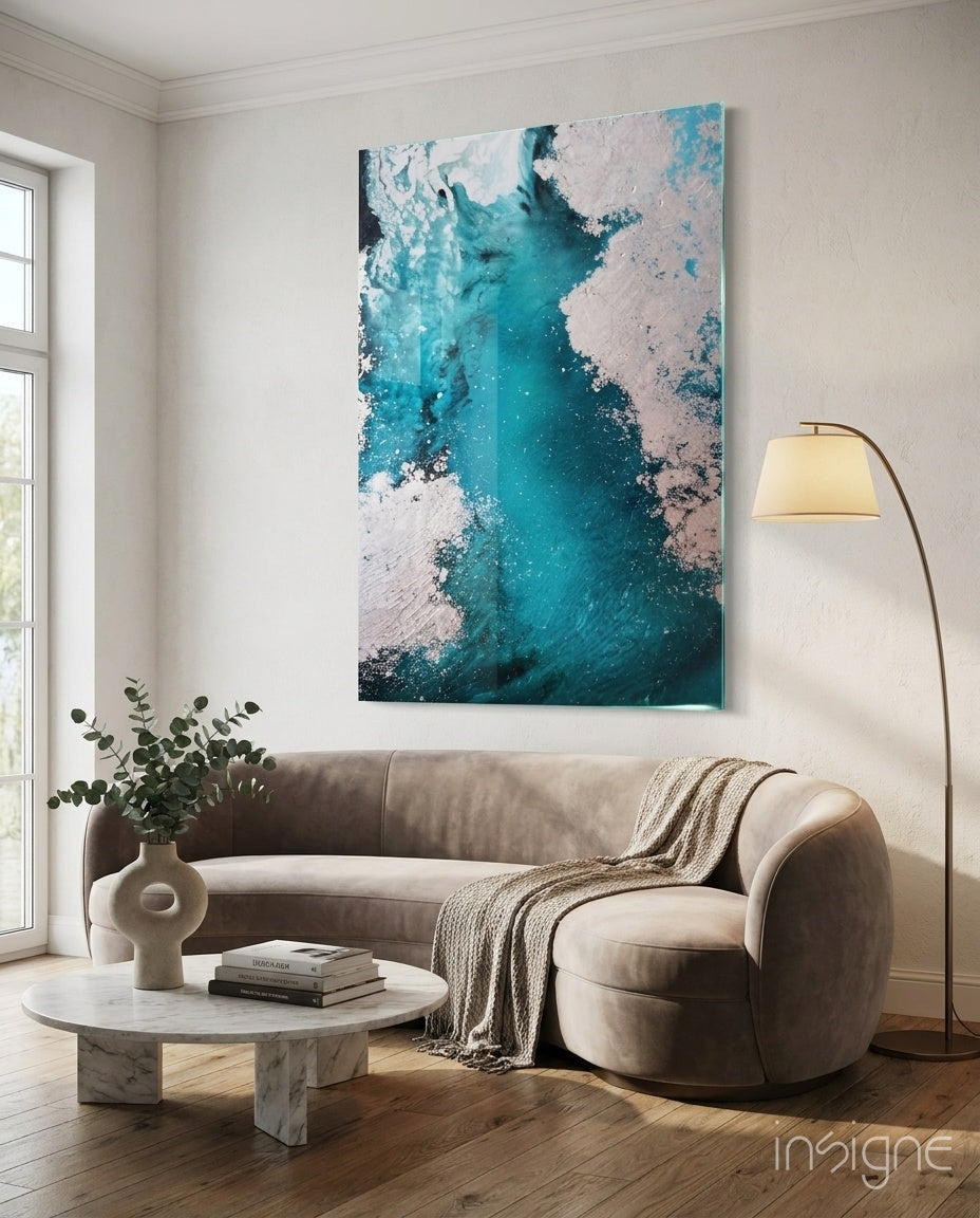 Colors of Abstraction glass wall art displayed above a beige curved sofa in a soft white-plaster lounge with marble coffee table and eucalyptus vase
