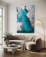 Colors of Abstraction glass wall art displayed above a beige curved sofa in a soft white-plaster lounge with marble coffee table and eucalyptus vase
