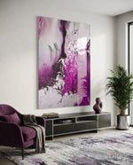 Colors of Abstraction glass wall art displayed above a black TV console in a soft white-walled lounge with plum velvet armchair and palm vase