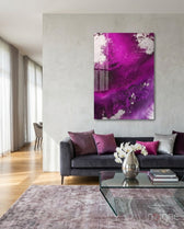 Colors of Abstraction glass wall art displayed above a charcoal velvet sofa in a soft white-plaster lounge with magenta and silver pillows