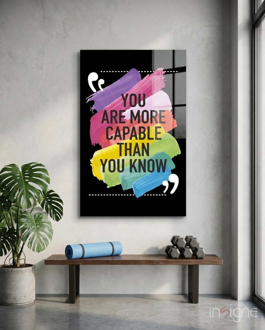 You Are More Capable glass wall art displayed above a wood bench in a soft white-plaster studio with monstera and yoga mat