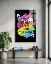 You Are More Capable glass wall art displayed above a wood bench in a soft white-plaster studio with monstera and yoga mat