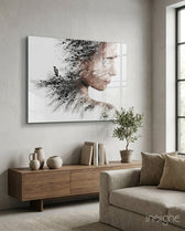 Woman Bird glass wall art displayed above a wood credenza in a soft white-plaster lounge with linen sofa and olive tree