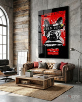 Bad Dog glass wall art displayed above a brown leather Chesterfield in a concrete-walled industrial lounge with reclaimed wood coffee table and Eames chair