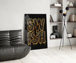 gold Swish basketball typography glass wall art leaning beside a dark leather sofa