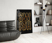 gold Swish basketball typography glass wall art leaning beside a dark leather sofa