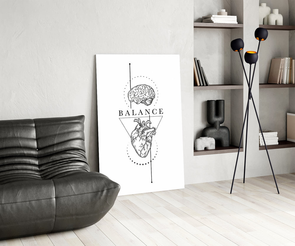 brain above heart balance line art glass wall art leaning beside a dark leather sofa