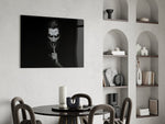 a grinning pale figure calling for silence glass wall art leaning beside a dark leather sofa