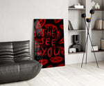 a red handwritten warning over watching eyes glass wall art leaning beside a dark leather sofa