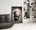stencil girl releasing red paper cranes glass wall art leaning beside a dark leather sofa