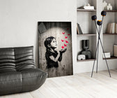 stencil girl releasing red paper cranes glass wall art leaning beside a dark leather sofa