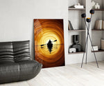 a lone kayaker at golden sunset glass wall art leaning beside a dark leather sofa