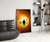 a lone kayaker at golden sunset glass wall art leaning beside a dark leather sofa