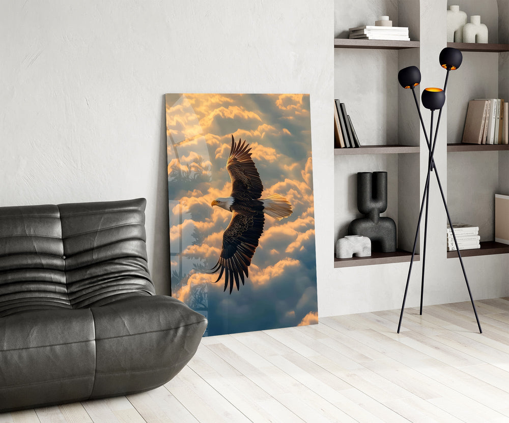 a bald eagle soaring above golden clouds glass wall art leaning beside a dark leather sofa