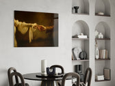 two hands reaching in golden light glass wall art leaning beside a dark leather sofa