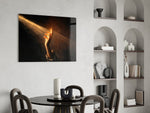 a hand reaching into a golden light beam glass wall art leaning beside a dark leather sofa