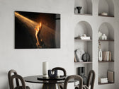a hand reaching into a golden light beam glass wall art leaning beside a dark leather sofa
