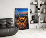 twilight aerial view of an illuminated mosque glass wall art leaning beside a dark leather sofa