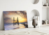 Close-up detail of weathered pier posts and driftwood in amber surf