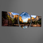 A panoramic mountain valley with golden-lit granite cliffs, a winding river, and a dense pine forest under a dramatic blue sky. 3 piece glass wall art set E