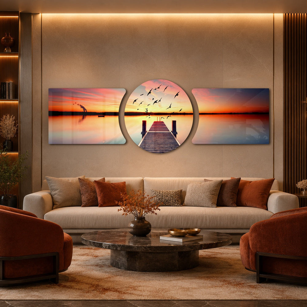 A wooden pier reaching into a calm lake at sunset with a flock of birds taking flight across a fiery orange sky. 3 piece glass wall art set C