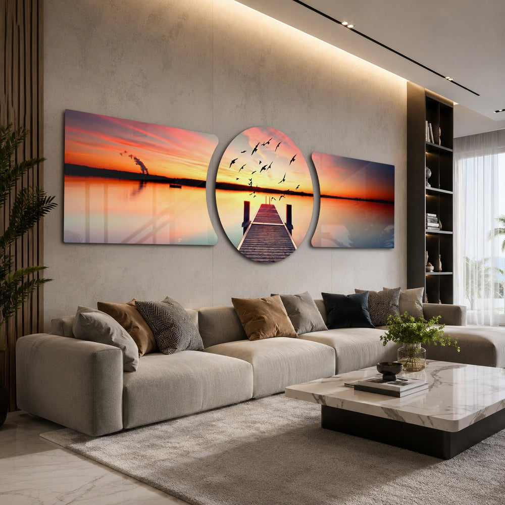 A wooden pier reaching into a calm lake at sunset with a flock of birds taking flight across a fiery orange sky. 3 piece glass wall art set D