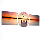 A wooden pier reaching into a calm lake at sunset with a flock of birds taking flight across a fiery orange sky. 3 piece glass wall art set E
