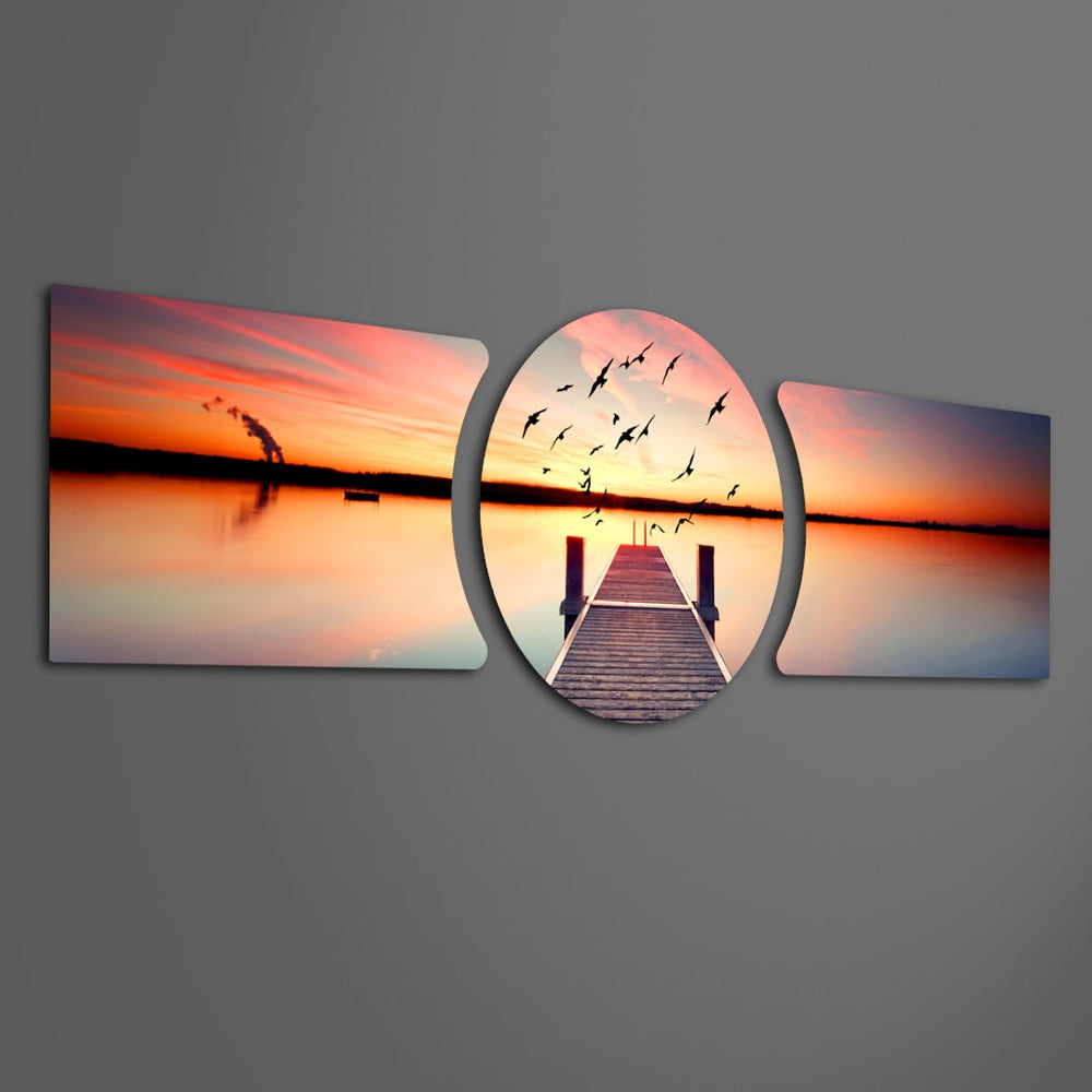 A wooden pier reaching into a calm lake at sunset with a flock of birds taking flight across a fiery orange sky. 3 piece glass wall art set F