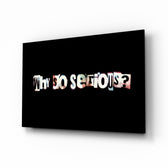 Why so Serious glass wall art displayed above a charcoal sofa in a slate-walled office lounge with steel desk and matte-black shelving