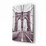 Brooklyn Bridge glass wall art displayed above a linen bed in a dusk-mauve bedroom with rattan nightstands and brushed-brass sconces