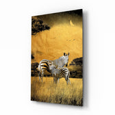 Zebras glass wall art displayed above a linen sofa in a warm safari lounge with rattan armchair and brass picture light