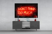 Don't Think Too Much glass wall art catching light to reveal its painted neon glow